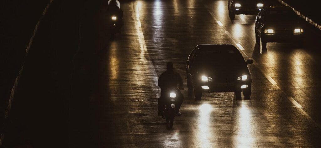 Nachtverkehr mit Fahrzeugen und Motorradfahrer / mostafa_meraji