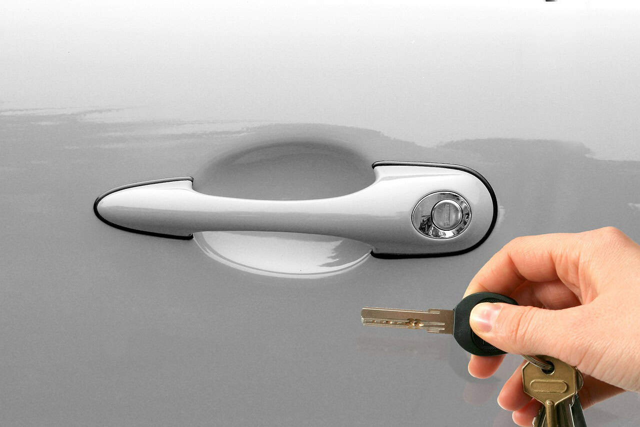 Hand mit Autoschlüssel am Türgriff.